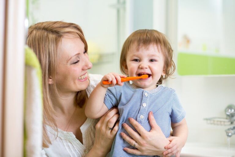 mother teaching toddler son teeth brushing in bathroom