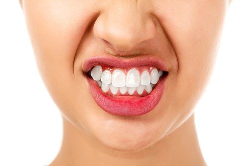 Woman's mouth with clenched teeth and a white background.