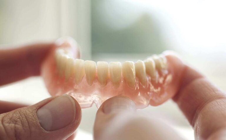 Close-up of hands holding dentures near window