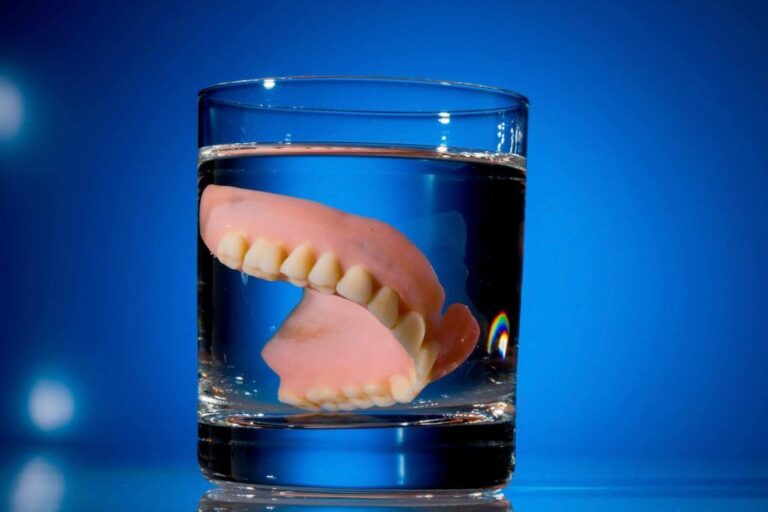 Dentures in glass of water, blue background