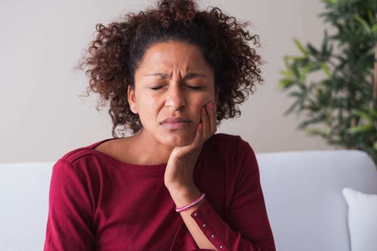 Woman wearing red shirt holding side of face near mouth in pain