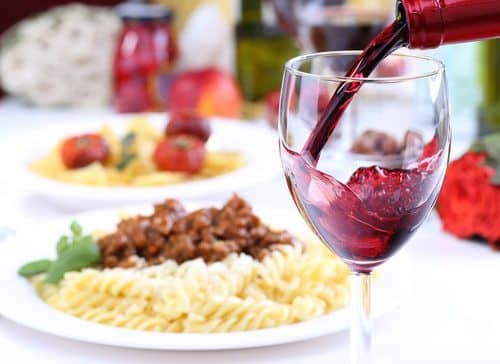 pouring a glass of red wine, pasta in background