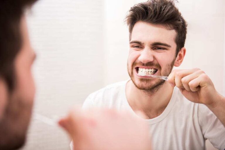 Young man looking in mirror while brushing his teeth