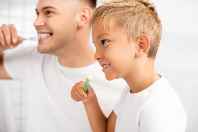 Smiling-boy-about-to-brush-his-teeth-looking-at-young-man-brushing-his-teeth