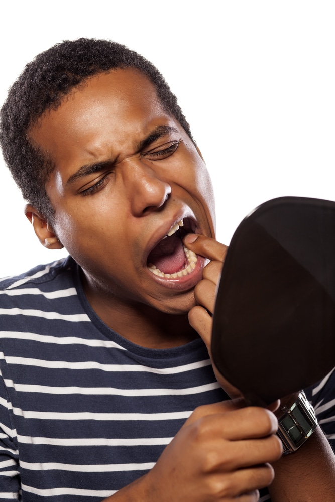 Man stretching mouth, looking in mouth with mirror