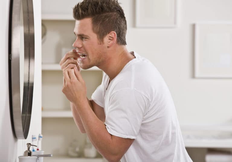 Young man flossing while looking in mirror