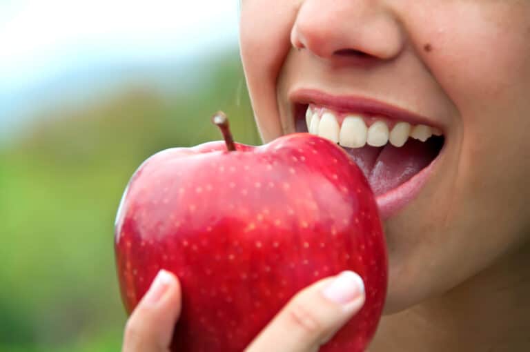 Close-up of woman biting into red apple outside
