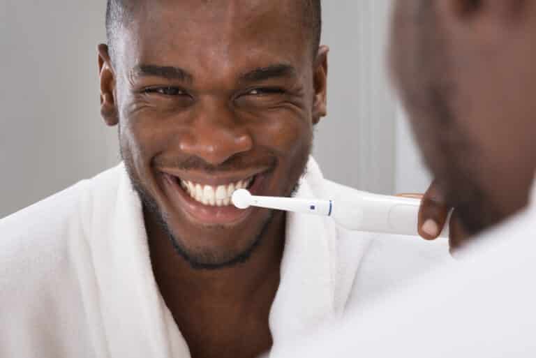 teeth with an electric toothbrush, looking in mirror