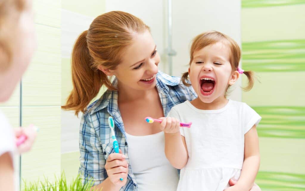 Young mother and young daughter smiling and brushing their teeth