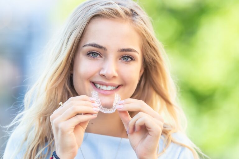 Smiling young woman putting in invisalign tray outdoors