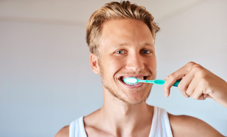 Young blonde man brushing his teeth