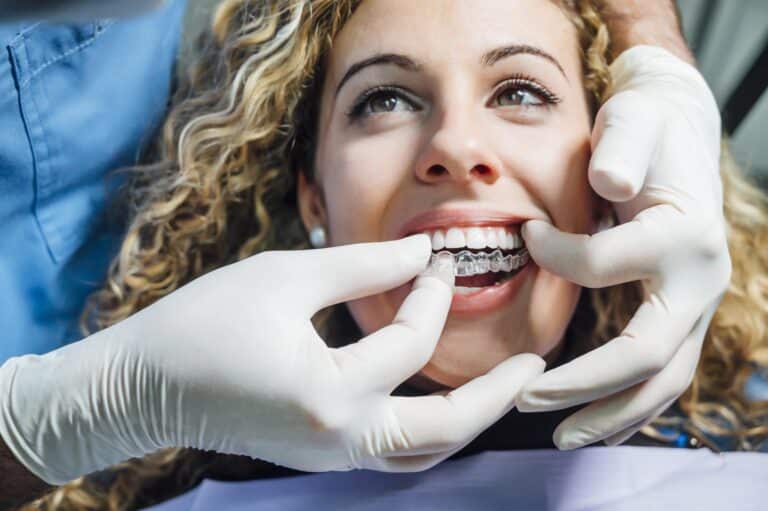 Dentist putting clear Invisalign aligners on teeth of a young woman