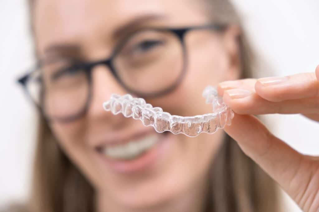 Smiling young woman holding up Invisalign aligner