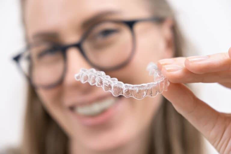 Smiling young woman holding up Invisalign aligner