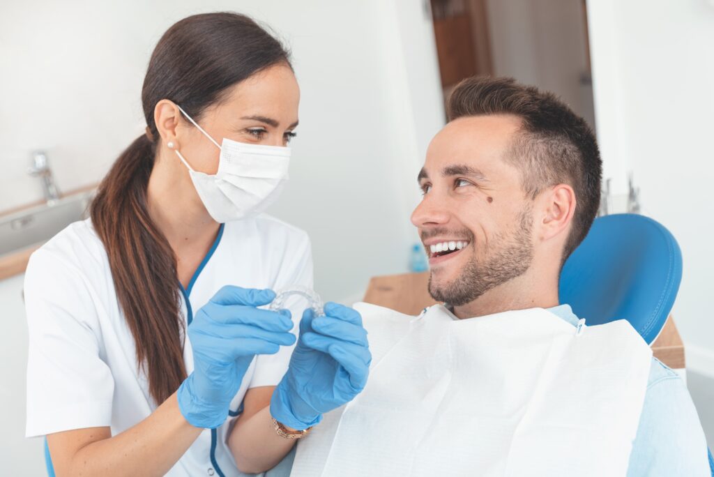 Young female dentist showing young male patient Invisalign aligners, both smiling