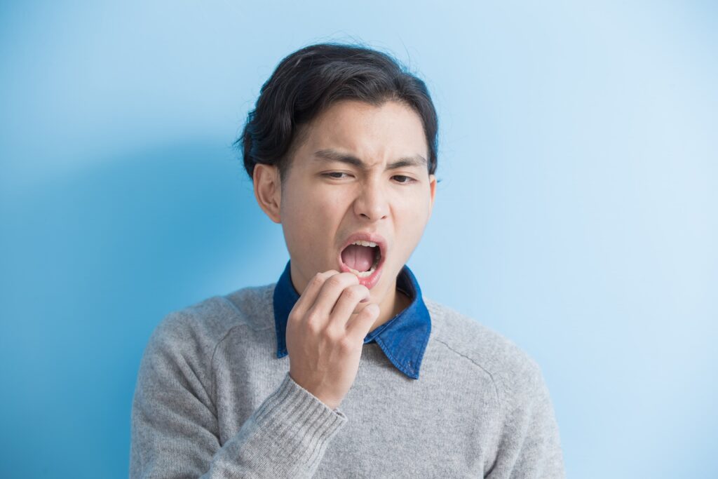 Young man with uncomfortable expression, holding hand to mouth